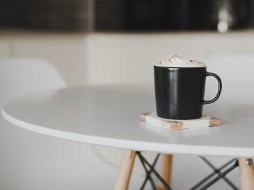 Coffee with whipped cream and cinnamon powder served in a black mug on a marble coaster
